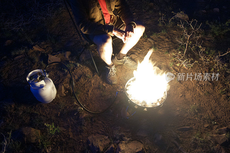 营地里，一名男子坐在丙烷火坑旁