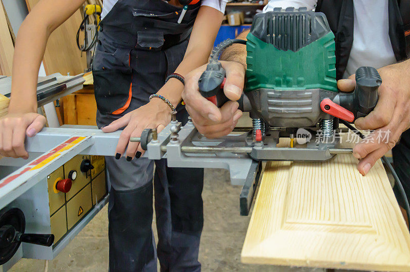 女木匠和男同事在木工车间使用磨砂机。