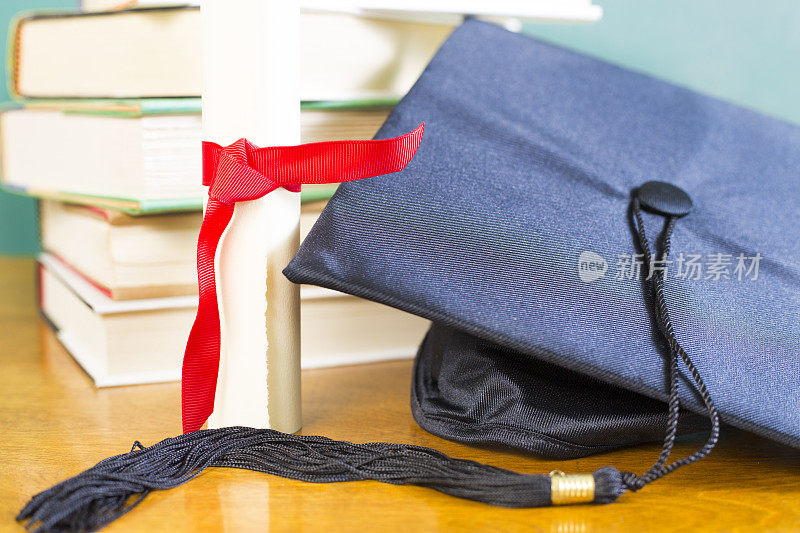 粉笔板背景与学位帽，教科书和文凭在一个抛光的木桌。绝佳的复印空间。