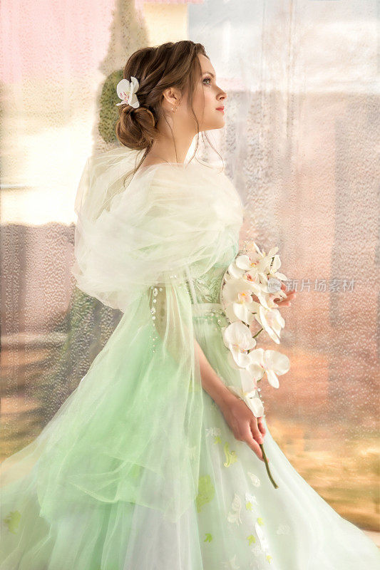 带着花和兰花的美丽少女。一个年轻女孩的肖像，穿着透明的裙子，绿色的眼睛和黑色的头发。童话艺术摄影