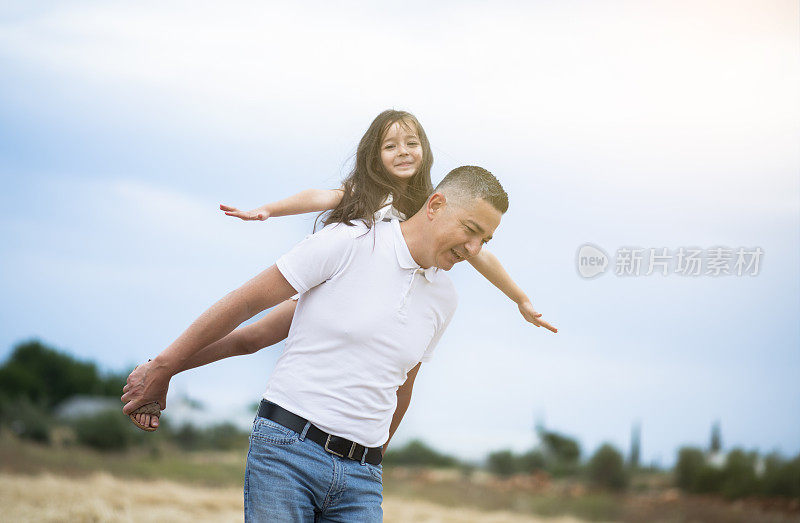 父亲节。可爱的小女孩骑在她爸爸的背上。爸爸和可爱的小女孩在一起玩