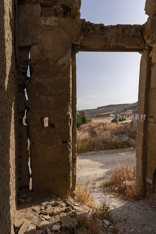 空空的门口和被风化的泥砖废墟的缝隙让人瞥见墙外的农村地区