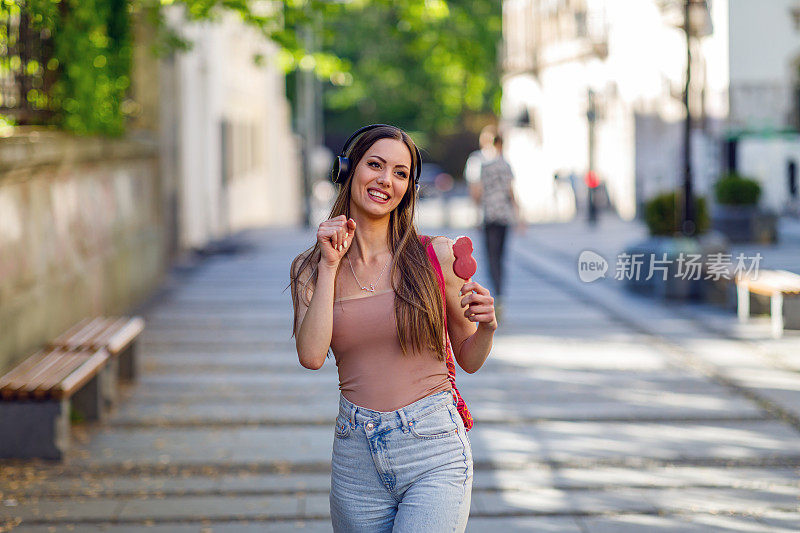 漂亮的年轻女子在街上拿着冰淇淋，微笑着，玩得很开心。