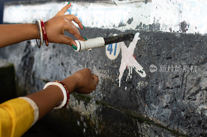 水资源短缺，一名印度妇女在公共场所从便签上拿着干净的水。