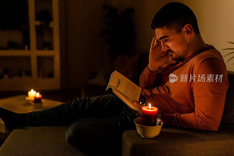 一个年轻人在家里遭遇电力危机，正在看书。