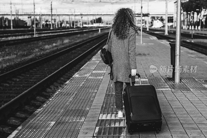 迁移。在火车站带着行李箱的红发卷发女孩。黑白色的摄影
