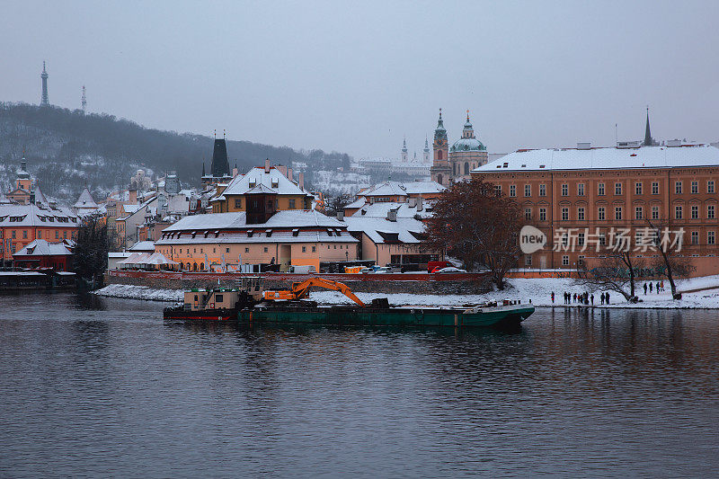 在冬季阴沉的天气里，河上的货船在镇岸边航行