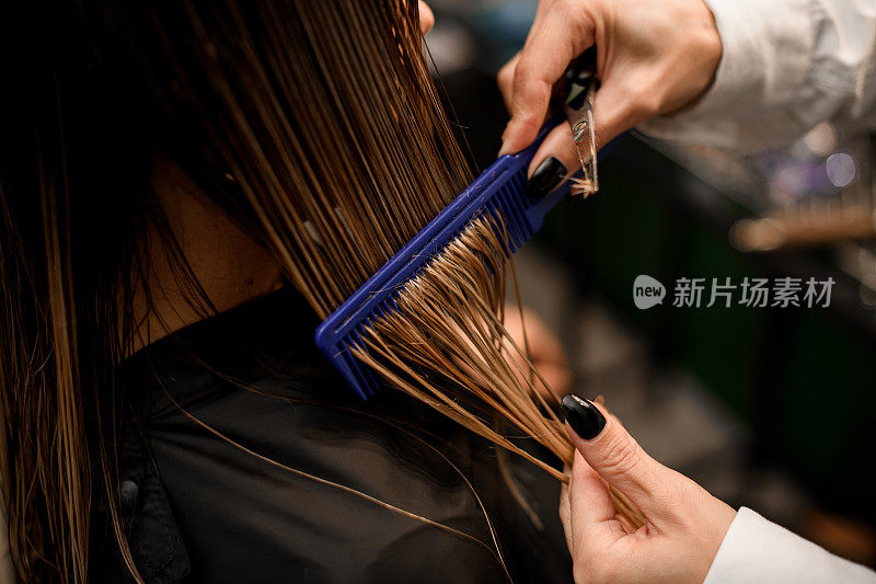 美发师的手与梳子和剪刀在理发过程中的健康女性头发在沙龙。