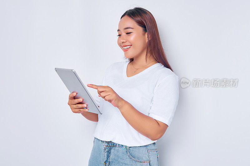 肖像微笑年轻的亚洲女孩在白色t恤使用数字平板隔离在白色背景