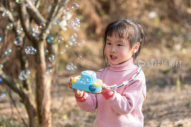 一个小女孩在梅园里用玩具吹泡泡