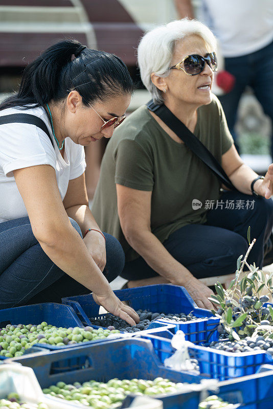 老年妇女和成年妇女在农贸市场购买新鲜橄榄的照片。