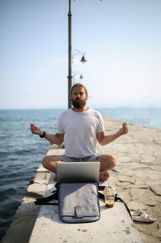 数码游民坐在沙滩上，拿着笔记本电脑在岸边沉思