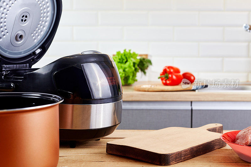 现代厨房餐桌上的菜板和多功能炊具。家庭厨房的电炖锅和食物。自动slo-cooker。