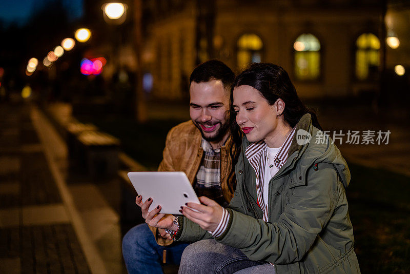 年轻的情侣在夜间散步时一起享受数码平板电脑