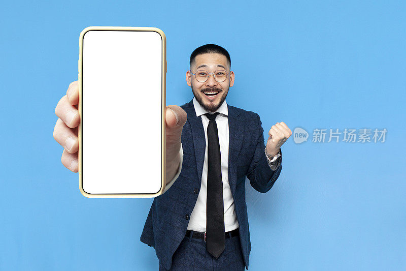西装革履的亚洲成功商人获胜者在蓝色孤立的背景上展示空白的智能手机屏幕