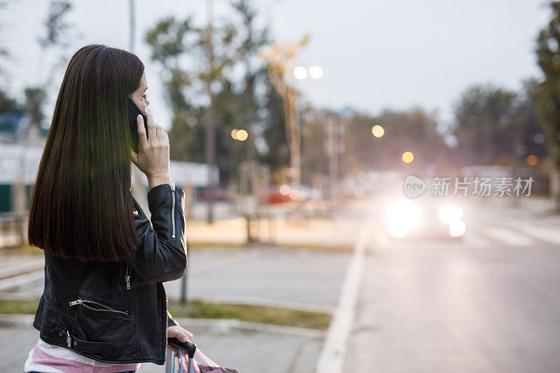 一个年轻女子站在人行道上，叫了一辆出租车，出租车从后面开来