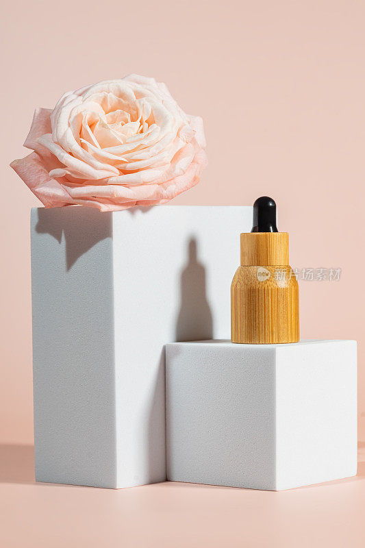 方形讲台上的化妆面油瓶上有粉红色的玫瑰。有机精华液，护肤品，天然化妆品品牌。模拟了