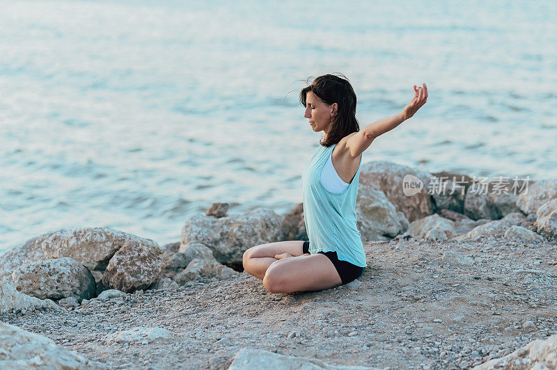 苗条的女人在海岸线练习瑜伽时伸展肌肉。