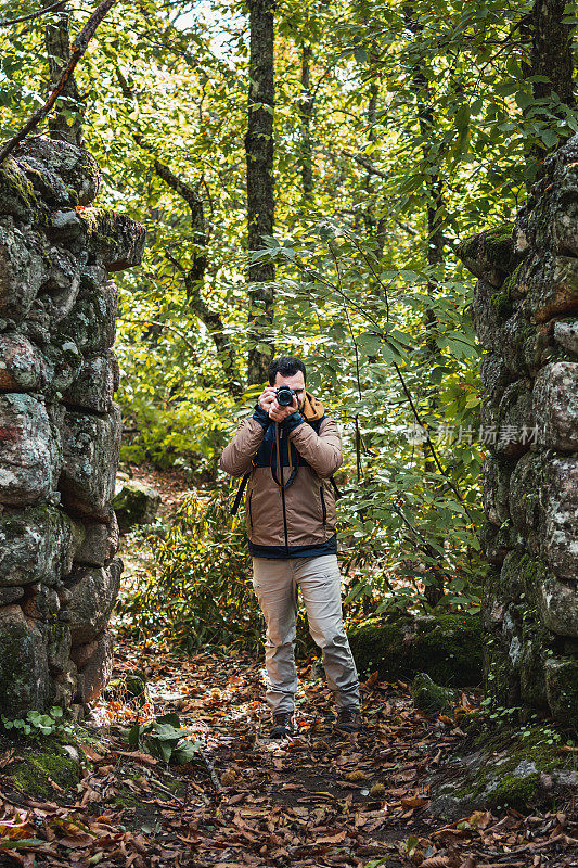 年轻美丽的摄影师从森林里的老石门拍了一张照片，看着相机，垂直照片