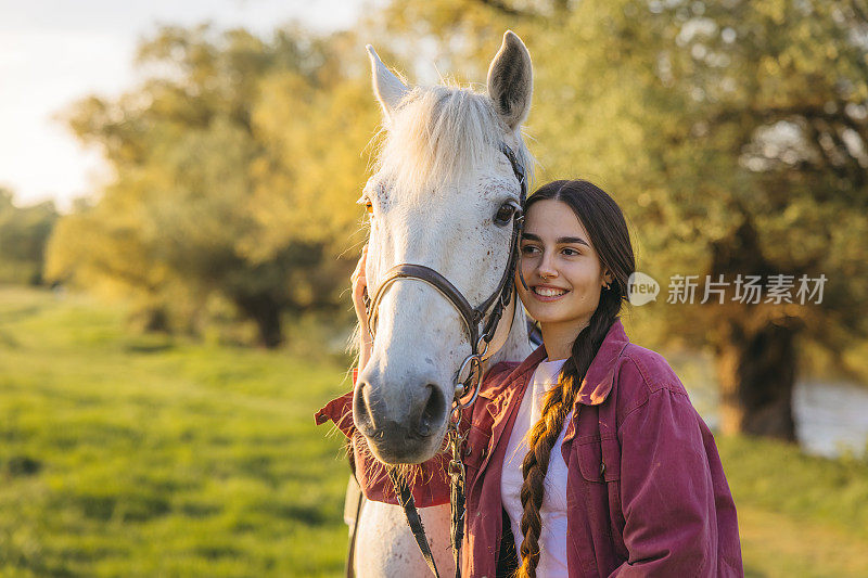 一个微笑的长发年轻女子在户外抚摸着她的白马