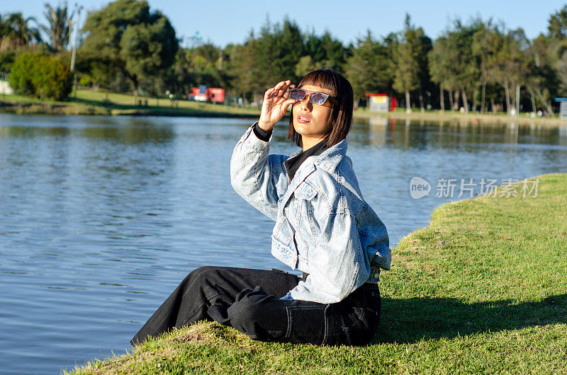 在一个阳光明媚的日子里，一名剪短头发的年轻女子在公园里穿着休闲服，戴着太阳镜