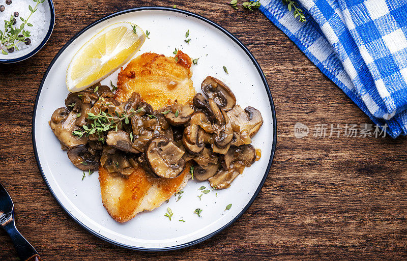 法式面包屑鸡肉牛排配蘑菇和洋葱酱配白葡萄酒，柠檬和百里香，质朴的餐桌背景，俯视图