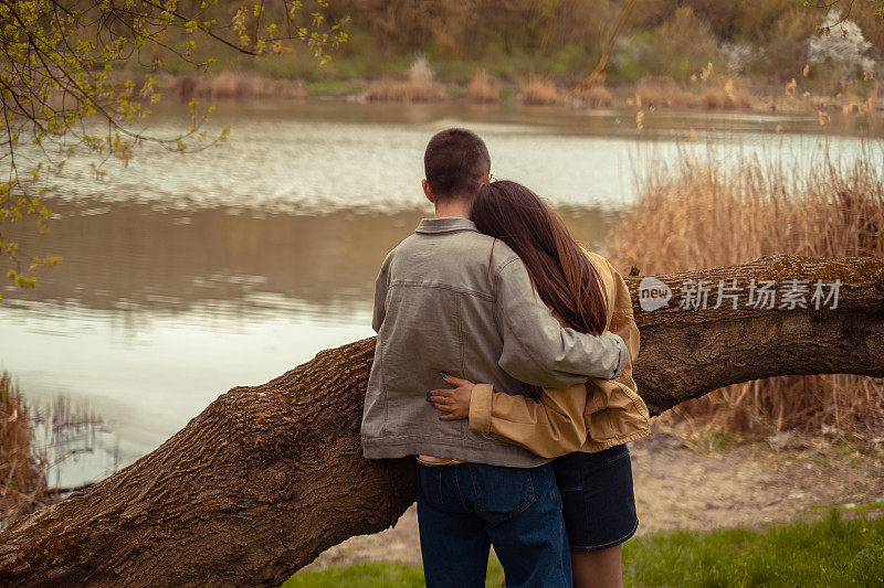 一个男孩和一个女孩在湖边拥抱，在大自然中享受野餐，反映了青少年的关系和友谊，拥抱积极的生活方式。情人节