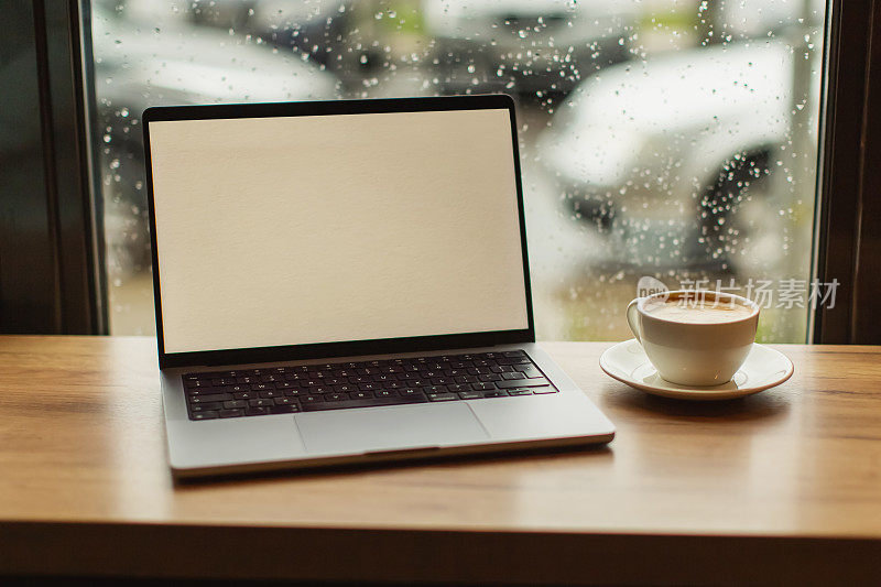 笔记本电脑和一杯咖啡放在靠窗的桌子上。