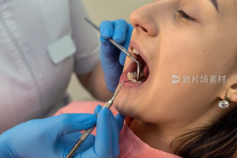 女牙医用牙科镜和不锈钢工具检查病人的牙齿
