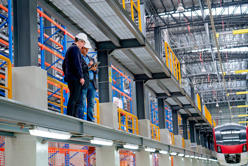 在工厂的工作场所，专业技术人员和工程人员站在铁轨附近的电力或地铁列车前。
