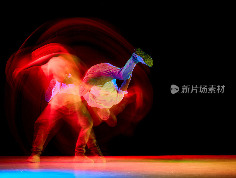 年轻的运动员，跳街舞的b-boy，一只手跳霹雳舞，在霓虹灯的黑色背景下抬起腿