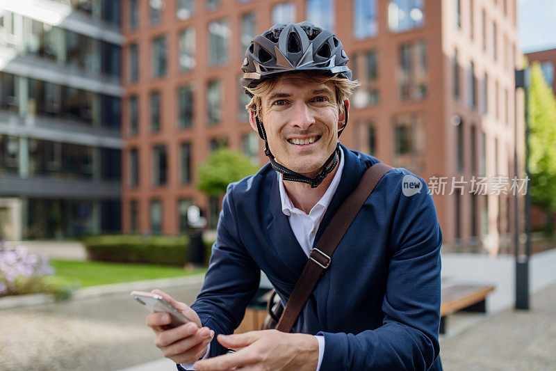 英俊的中年男子穿着西装，拿着智能手机，骑着自行车在城市里穿梭。在漫长的工作日后骑自行车下班的男性城市通勤者。