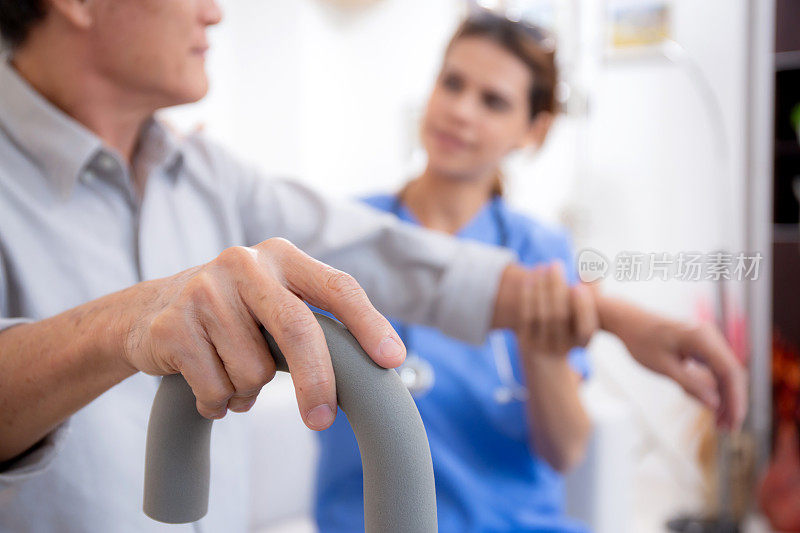 护理人员或护士照顾和支持老年患者在家中客厅拄着拐杖走路，物理治疗和保健，锻炼康复，医疗和保险。