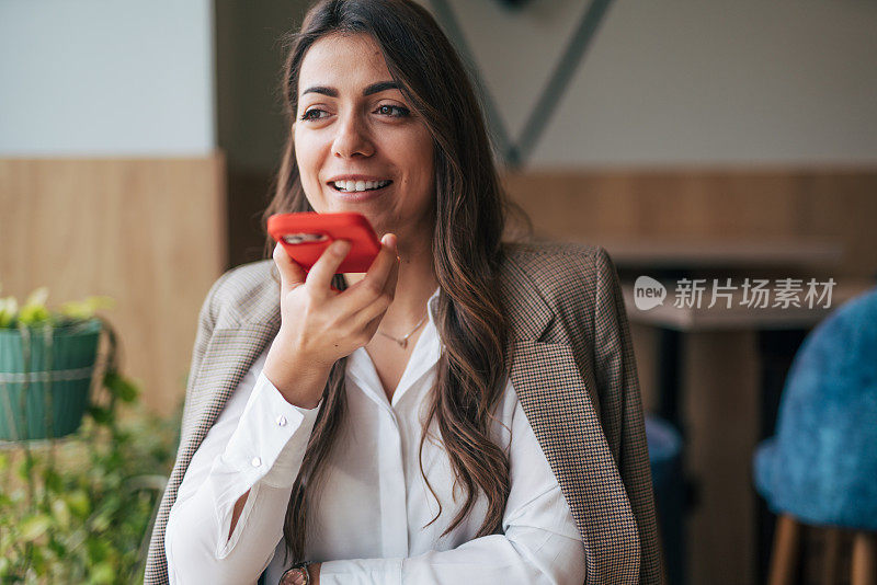 漂亮的年轻女子在咖啡馆边喝咖啡边用智能手机聊天