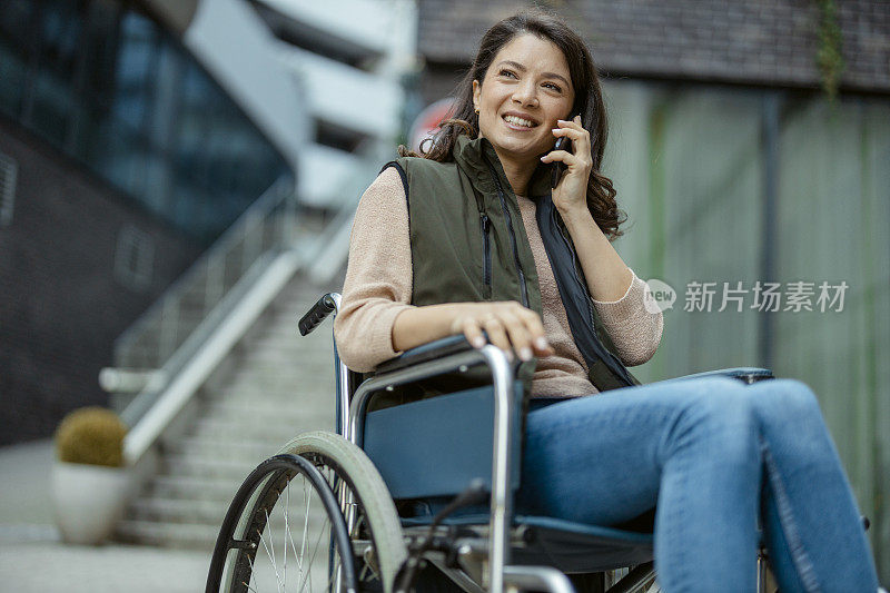 坐在轮椅上的残疾女性用智能手机与他人交谈