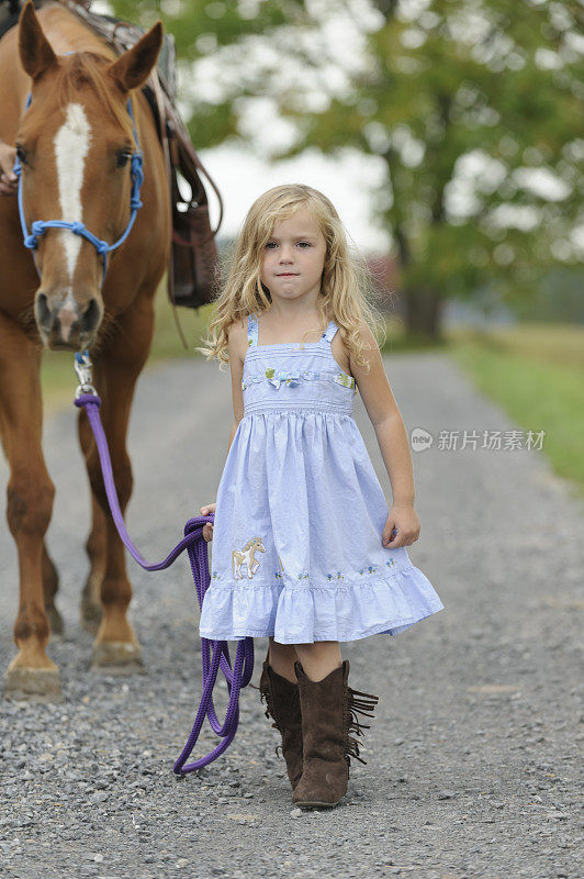 小女孩牵着大马走在乡间小路上