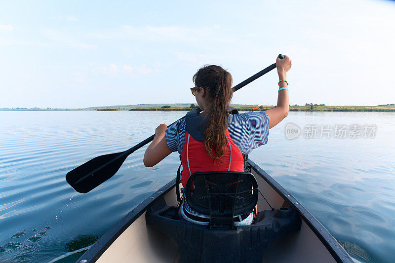 夏日里，年轻女子在湖中划独木舟。