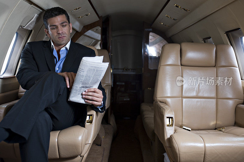 富裕的旅行-商人在商务飞机上阅读报纸