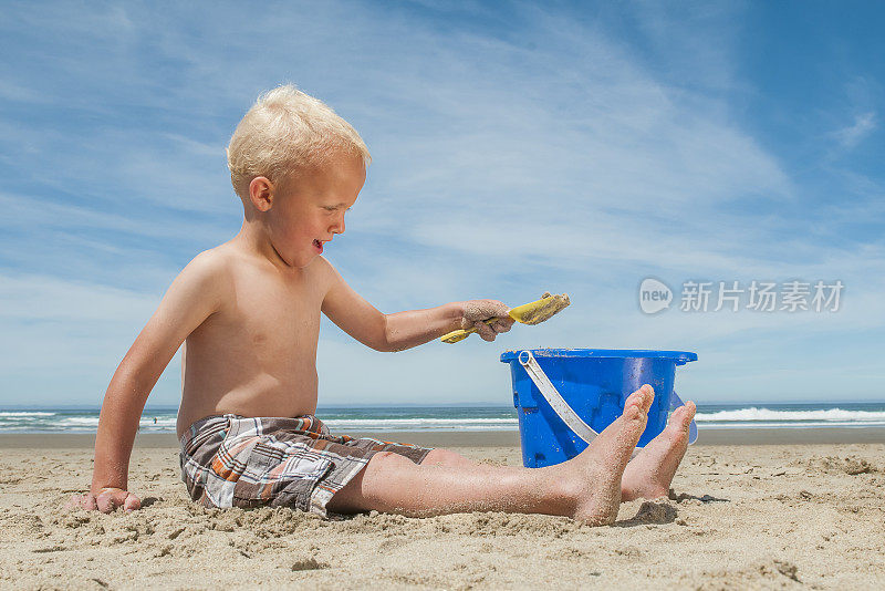 小男孩在沙滩上玩水桶。