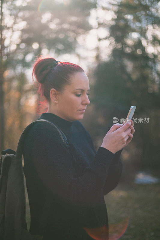 微笑的年轻女子在看她的智能手机户外照片上的信息