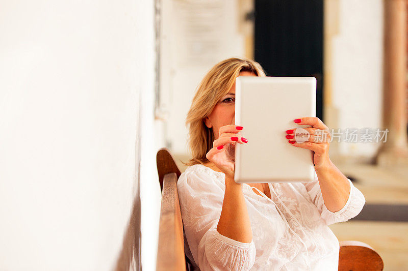成熟的金发美女用平板电脑拍照