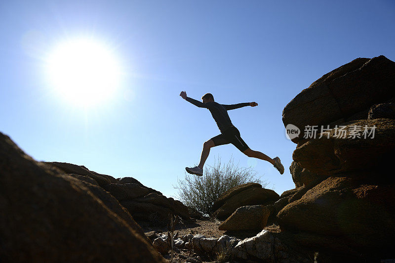剪影越野跑者从一块岩石跳到另一块岩石
