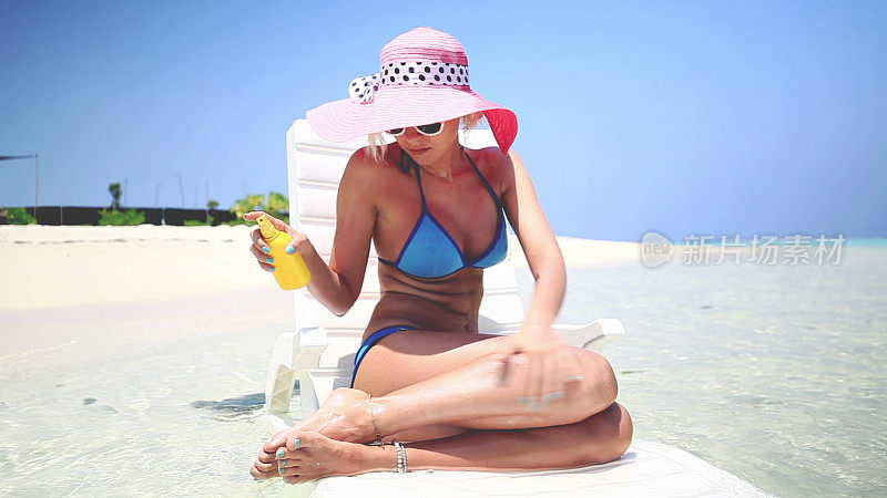 一名金发女子坐在马尔代夫的浅水中，涂抹日光浴霜