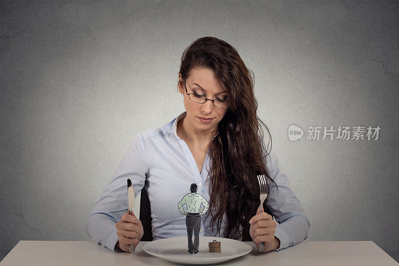 肖像年轻女子坐在餐桌前的一个盘子，看着一个小小的男人孤立在灰色的墙壁背景