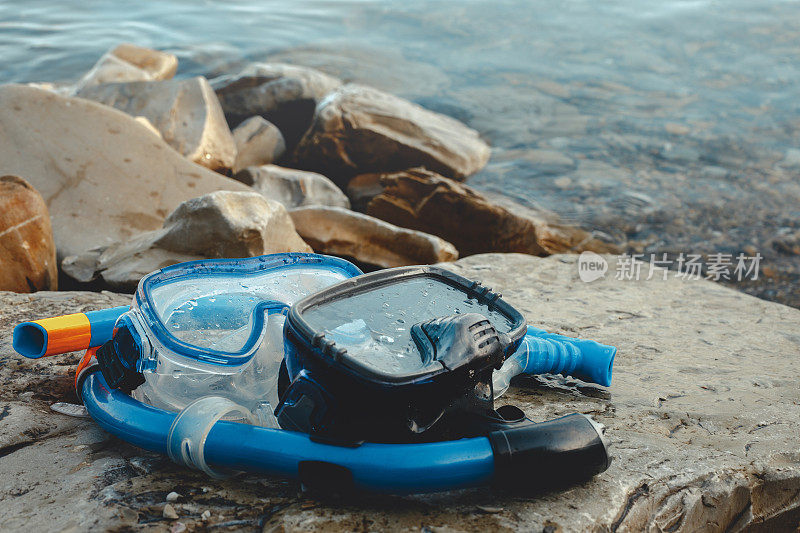 两个潜水面具和管道躺在海滩上，在岩石上。旅游与旅游概念