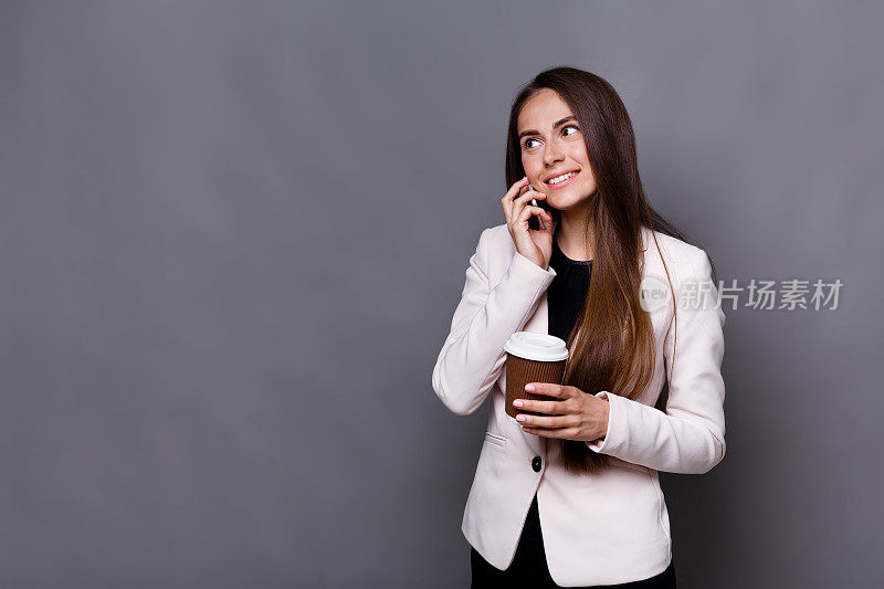 微笑的商务女性讲手机和喝咖啡在工作