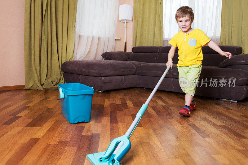 男孩在房间里打扫地板。男孩帮助妈妈打扫卫生。