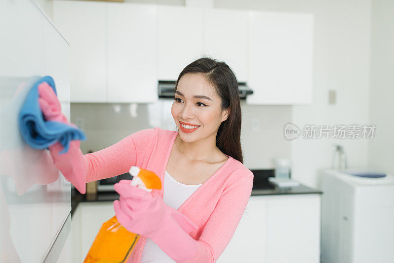 美丽的亚洲年轻女子在保护手套清洁厨房橱柜