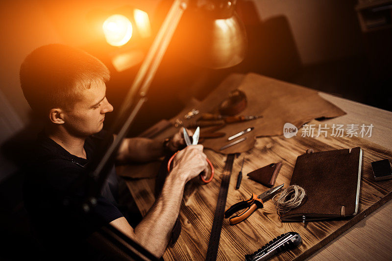 皮带在皮革车间的工作过程。手持制作工具的人正在工作。旧制革厂的皮匠。木桌上的背景。用于文本和设计的暖光