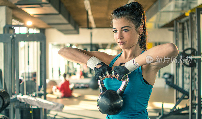 年轻健康的女人在健身房用水壶铃健身。